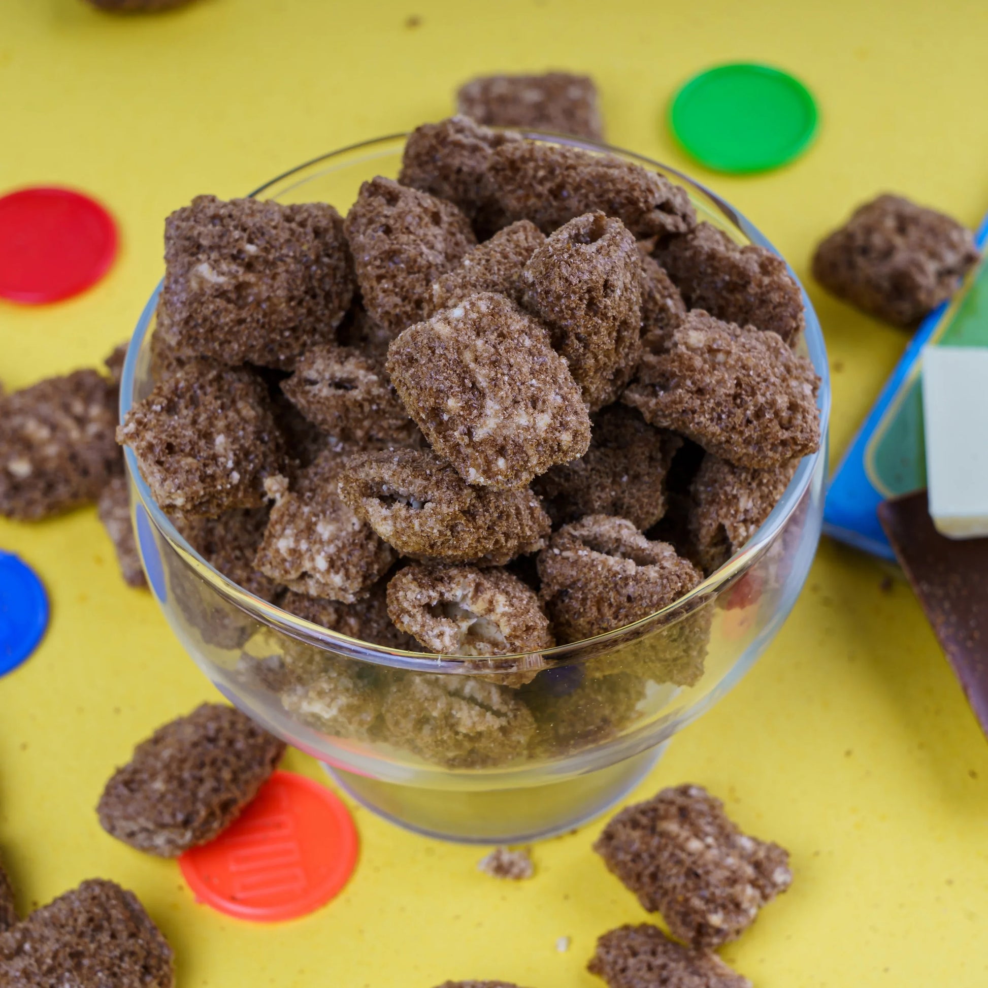 Crunchy jaggery-sweetened Indian snack cubes in glass bowl on yellow background with colorful caps