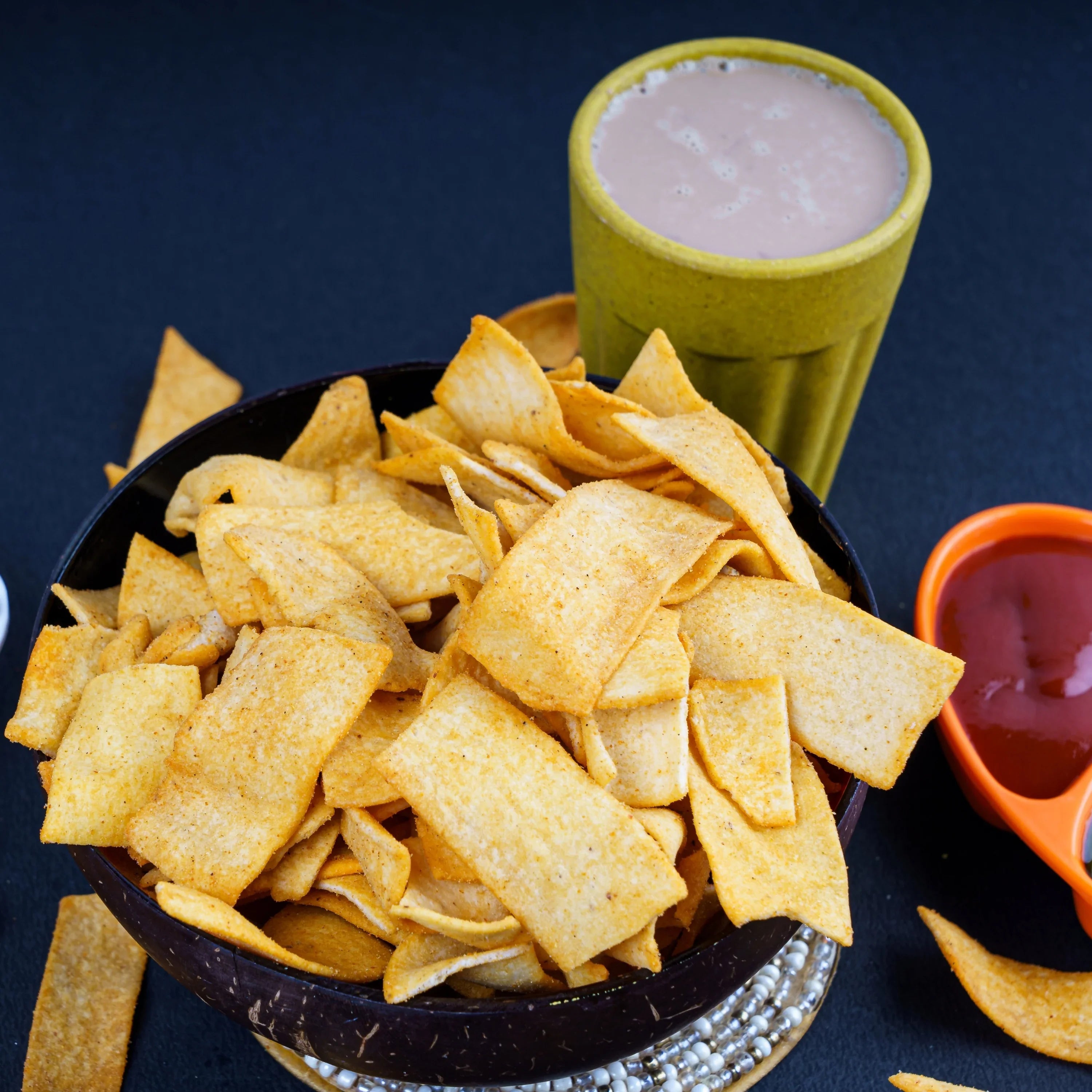 Crispy Indian-style chips in a bowl with pink drink and dipping sauce, clean label snacks