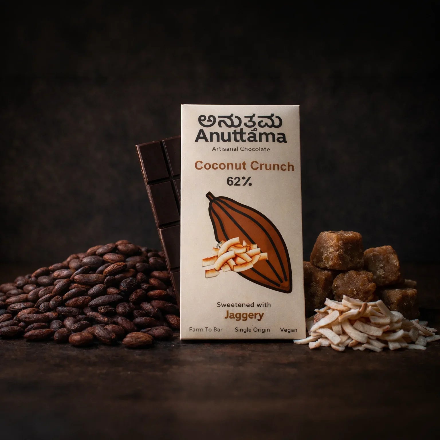 Anuttama Coconut Crunch 62% dark chocolate bar, sweetened with jaggery, surrounded by cocoa beans, coconut flakes, and jaggery cubes
