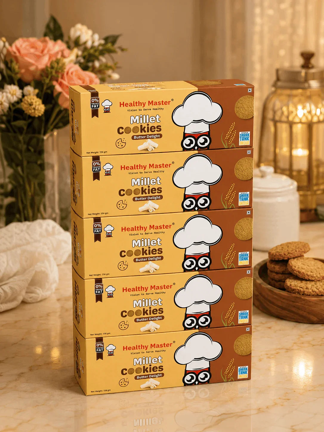 Healthy Master Millet Cookies Butter Delight boxes stacked on marble countertop with flowers and cookies nearby
